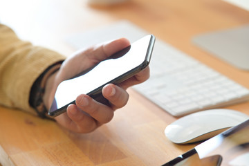 Fototapeta premium Man holding mockup mobile smart phone device on office workspace