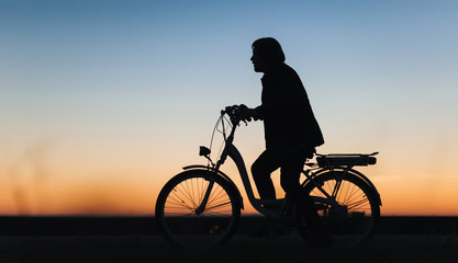 Fototapeta na wymiar Male cyclist on the e-bike or electric bicycle on the sunset background. Silhouette of the young man in profile. Active life. Travel. Sport.