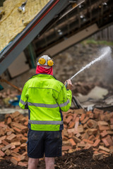 Workman spraying water over a demolition site to prevent dust and possible fire from the demolition process