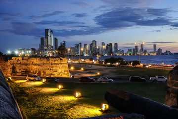 A panoramic view of the magical colonial city of Cartagena. The stone walls surrounds the old colonial part of the city with Spanish style and cannons. Also new city building and dusky sky, Colombia.