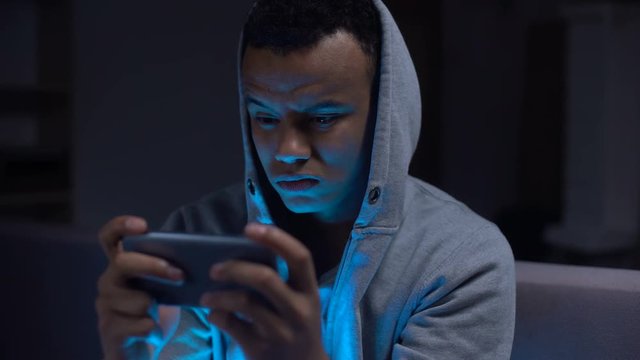 Unhappy african-american teenage procrastinator losing video game on smartphone
