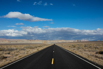 Black paved road in desert with yellow dotted line at ceter of frame