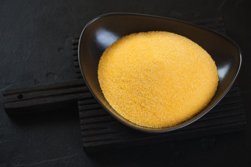 Black bowl with raw polenta on a black wooden background, studio shot