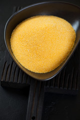 Uncooked polenta in a black bowl on a black wooden serving board, closeup, vertical shot