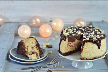Cheesecake with chocolate topping on a white plateau on a wooden background. A piece of cheesecake on a rustic plate