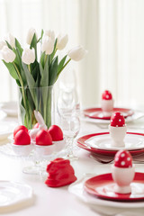 Happy easter. Decor and table setting of the Easter table is a vase with white tulips and dishes of red and white color. Easter colored eggs with white polka dots.