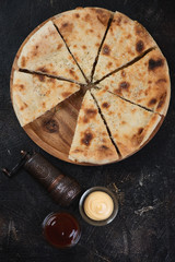 Sliced ossetian pie on a wooden serving tray, flatlay on a dark brown stone background, vertical shot
