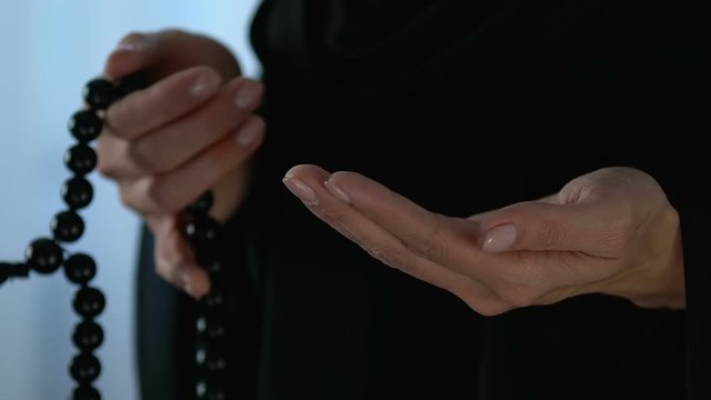 Female in hijab counting prayers by rosary in hand, faith and religion, close-up
