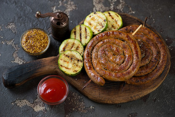 Rustic wooden serving board with grilled rolled sausages, zucchini and dipping sauces, studio shot