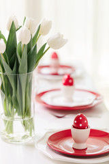 Happy easter. Decor and table setting of the Easter table is a vase with white tulips and dishes of red and white color. Easter colored eggs with white polka dots.