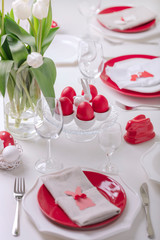 Happy easter. Decor and table setting of the Easter table is a vase with white tulips and dishes of red and white color. Easter colored eggs with white polka dots.