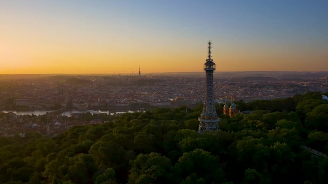 Aerial drone shot of Petrin tower in sunrise over the old town of Prague and Prague Castle.