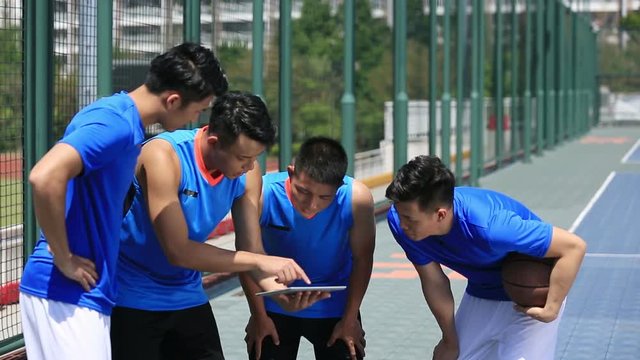 group of asian young adult basketball players discussing tactics using digital tablet.
