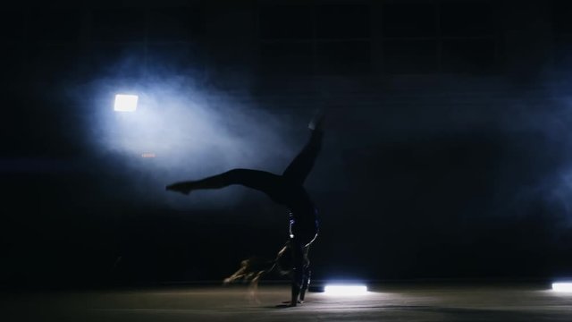 Talented girl gymnast performs flips on the gymnastics carpet in slow motion in the light in the smoke.