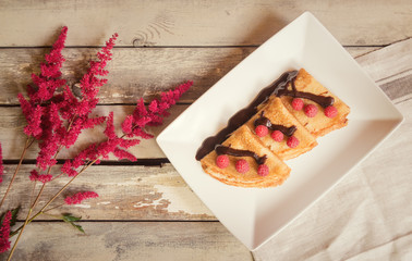 Homemade crepes with fresh raspberries and chocolate syrop and astilbe flowers on aged wooden...