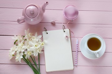 Fototapeta na wymiar Spring tea.Flat lay.Spring to-do list.cup of tea, empty notebook, white daffodils bouquet, pink teapot on pink board wooden background..top view, copy space.Spring mood