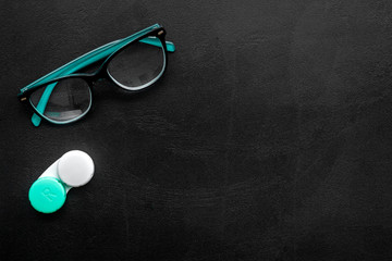 Eyes care. Glasses with transparent lenses and contact lenses on black background top view space...