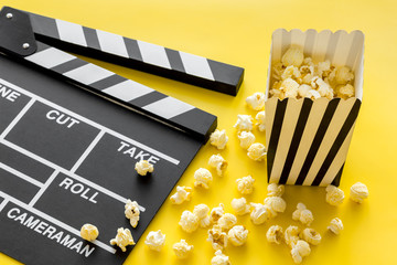 Movie premiere concept. Clapperboard and popcorn on yellow background