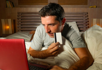 Fototapeta na wymiar young attractive and relaxed man at home bedroom lying on bed buying or banking online using credit card for paying in electronic business and commerce concept