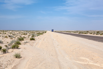 Passenger tourist coach driving in the distance in deserted highway in salt dried lake, road from Algeria to Tunisia on Chott El Jerid salt flat. Africa