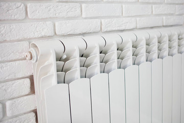 A White heating radiator on the brick plaster wall