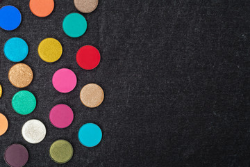 Obraz na płótnie Canvas set of many shimmer and matt multicolored circle shaped eye shadows lying on a black textile. concept of professional make up tools. free space for advertising