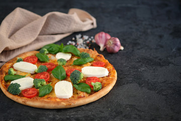 Italian pizza with Mozzarella cheese, tomatoes, broccoli, Spices and fresh basil. Pizza and kitchen napkin near, on black stone background