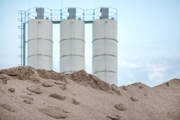 Obraz premium Large piles of construction sand and gravel used for asphalt production and building. Limestone quarry, mining rocks and stones. Factory in the background. Empty space for text of logo 