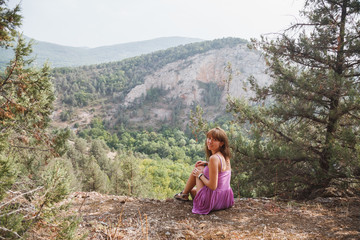 The girl is sitting on a rock. Down the river runs