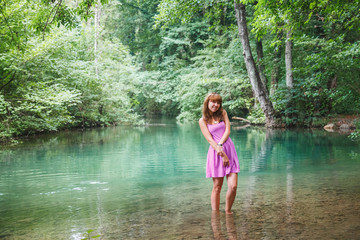 Fototapeta premium girl in a pink short dress walks on a river in the forest