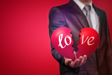 Crop image of a man in suit holding a big red broken heart with the word 'love' on red background.