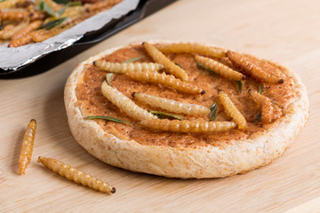 Food insects: Bamboo worm for eating as food. Bakery baked bread made of cooked insect and bamboo caterpillar in baking tray on wood background is good source of protein edible. Entomophagy concept.