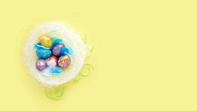colorful background for easter eggs in a nest with blue feathers. on a yellow background, pastel colors. basket of holiday treats.