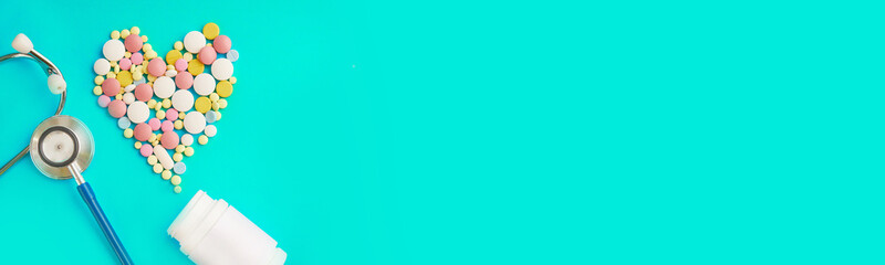 pills in a plastic jar and a stethoscope on a blue background in the shape of a heart. free space for text.