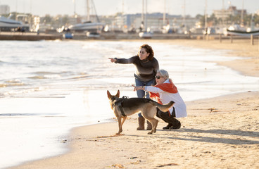 Beautiful older mom and mature daughter walking their german shepard dog on beach at autumn sunset