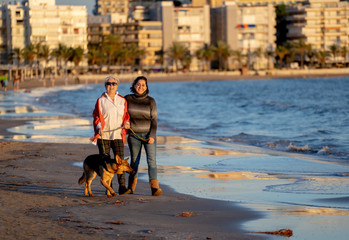 Beautiful older mom and mature daughter walking their german shepard dog on beach at autumn sunset