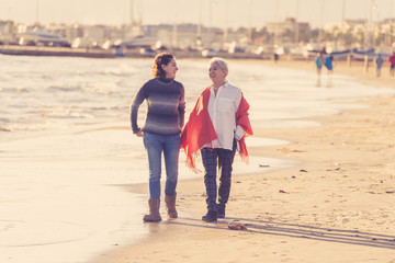 Portrait of beautiful older mom and mature daughter walking on the beach at autumn sunset