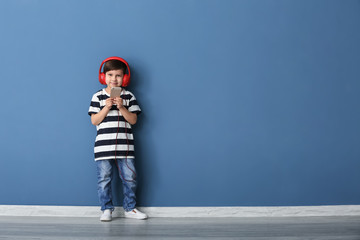Fototapeta na wymiar Portrait of cute boy with headphones and mobile phone near color wall