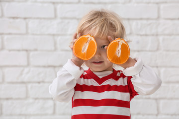 Fototapeta premium Portrait of cute little boy with halves of orange on white brick background