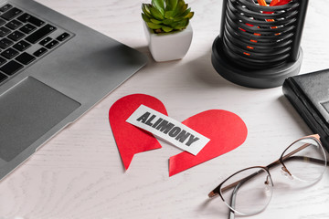 Broken heart, paper with text ALIMONY, glasses and laptop on table