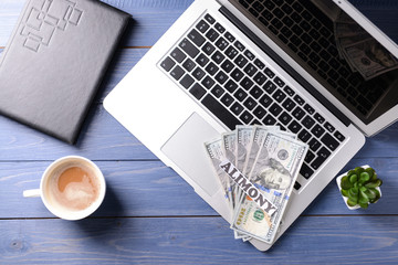 Fototapeta premium Laptop, money and paper with text ALIMONY on wooden table