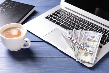 Laptop, money and paper with text ALIMONY on wooden table
