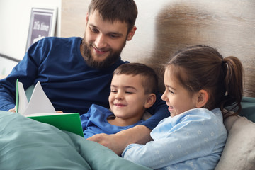 Young father reading book for his children in bed