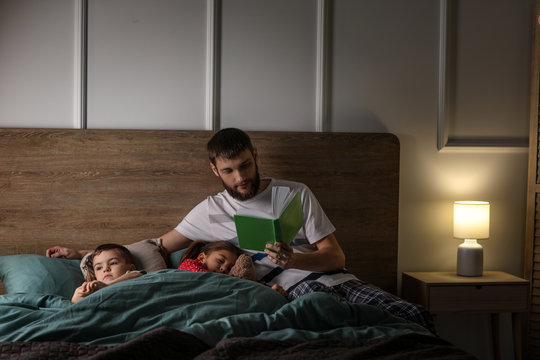 Young Father Reading Book For His Children In Bed