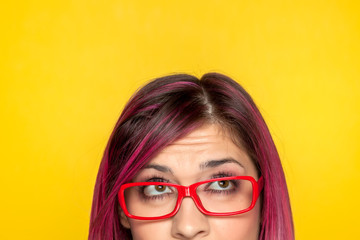 Half portrait of a young worried woman with pink hair and glasses on yellow background