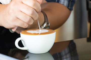 Barista drawing frothy art on milk in coffee cup for make latte art.