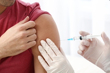 Doctor vaccinating male patient in clinic, closeup
