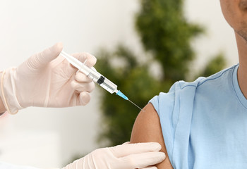 Doctor vaccinating male patient in clinic, closeup