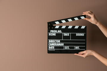 Female hands with cinema clapperboard on color background