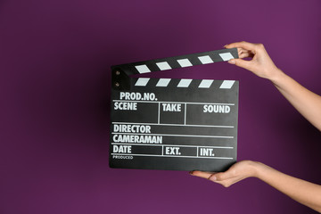 Female hands with cinema clapperboard on color background